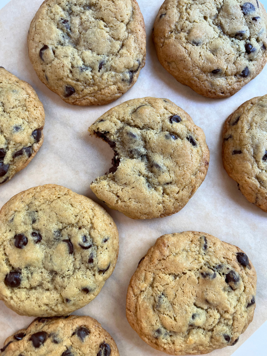 Close-up of freshly baked sourdough chocolate chip cookies on parchment paper, with one cookie showing a bite taken out to reveal the soft, gooey center