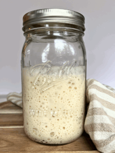 Glass jar filled with bubbly sourdough starter, showing an active and airy texture ready for baking.