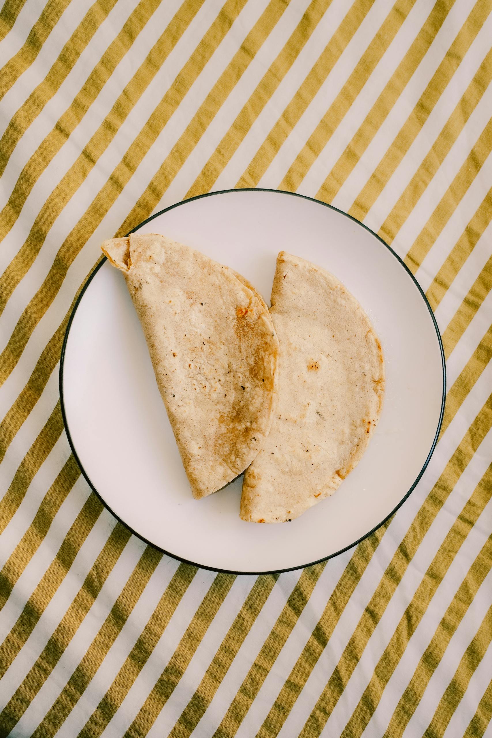 Two corn tortillas placed on a white plate, striped textile background.